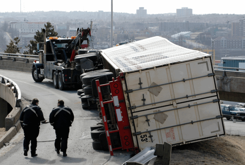 Image is of a flipped over semi-truck with city officials at the scene, concept of liability in truck accidents in Tennessee