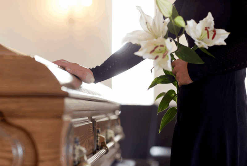 Image is of a mourning woman standing at a closed coffin with white flowers, concept of filing wrongful death claims after fatal accidents