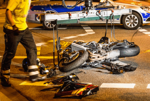 Image is of a wrecked motorcycle on the road with crews working to clean the debris, concept of what to do after a hit and run motorcycle accident in Nashville