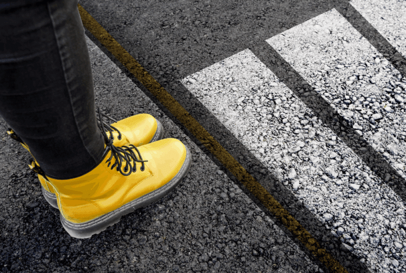 Image is of a woman's feet in yellow combat boots on a sidewalk about to walk into a pedestrian crosswalk, concept of Nashville pedestrian accident case