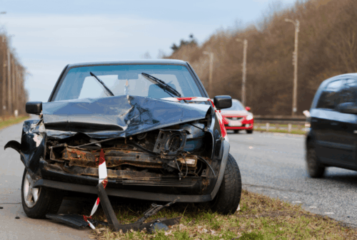 Image is of a smashed front end of a car on the side of a busy highway, concept of common mistakes after a car crash in Nashville