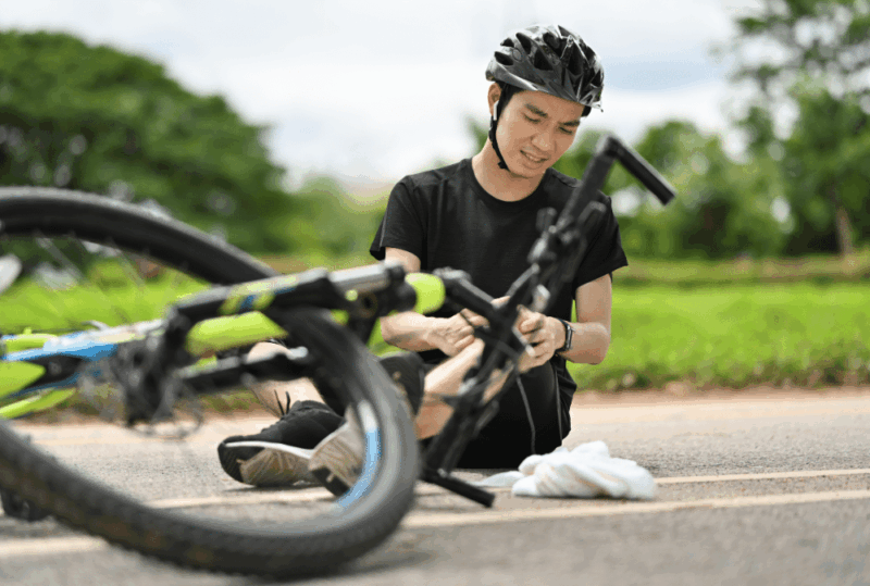 Image is of an injured cyclist looking at his leg while on the ground after an accident, concept of suing after being hit by car in Nashville