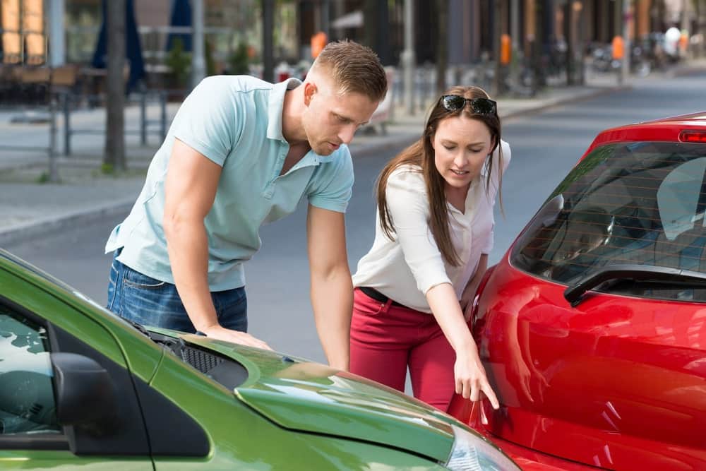Image is of two people pointing at damage on their vehicles after a collision, concept of gathering evidence to prove negligence.
