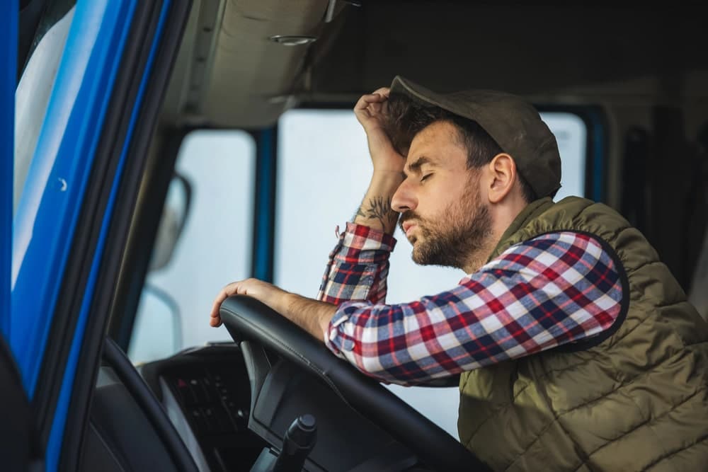 Image is of a visibly exhausted truck driver leaning on the steering wheel, concept of truck accidents in Nashville linked to severe fatigue.