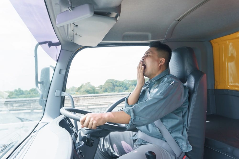 Image is of a tired truck driver yawning behind the wheel, concept of truck accidents in Nashville caused by fatigue and delayed reactions.