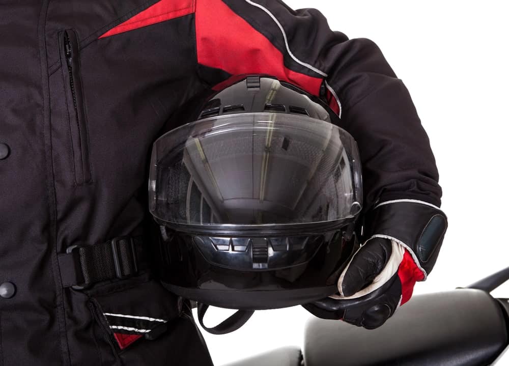 Image is of a motorcycle rider holding a protective helmet after riding, representing how helmet use can influence motorcycle accident claims and injury evaluations.