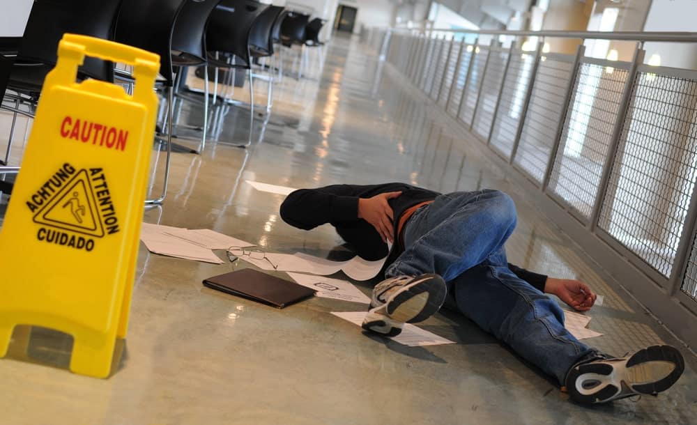 Image is of a person lying on the floor near a caution sign after a fall, showing the real world dangers involved in Tennessee slip and fall accidents.