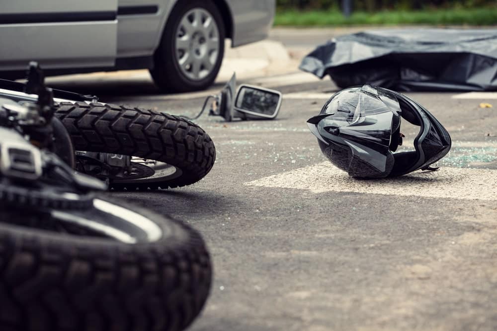 Image shows a damaged motorcycle, a fallen helmet, and broken glass on the roadway, illustrating the serious injuries and costs that result from a motorcycle crash in TN.