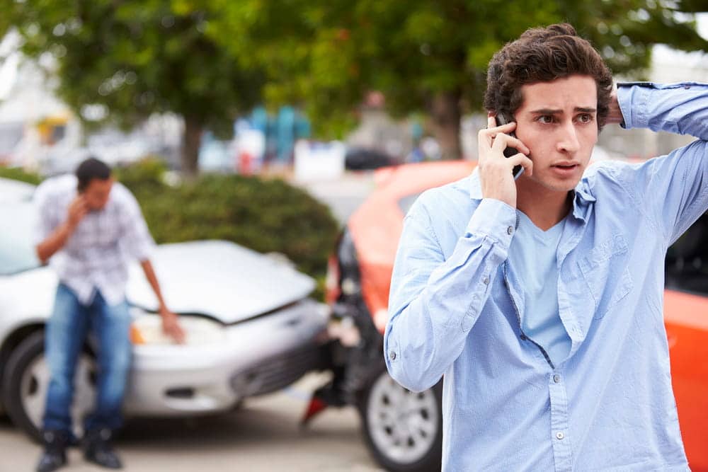 Image is of a stressed driver standing near damaged vehicles while speaking on the phone after a crash, illustrating how Tennessee’s comparative fault law applies in car accident situations where fault is disputed.