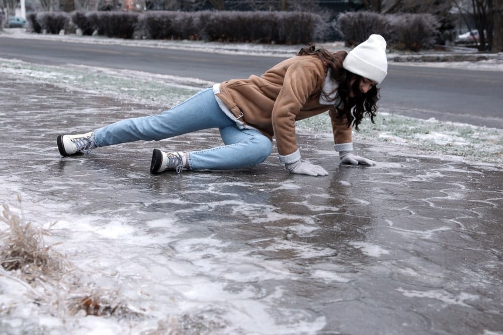 Image is of a woman slipping on an icy sidewalk, illustrating how winter conditions contribute to slip and fall injuries in pedestrian areas.
