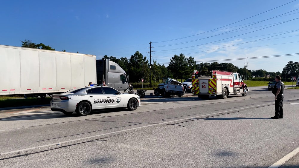 Image is of law enforcement officers and emergency vehicles at a truck crash scene, concept of fault in truck accidents and official investigation evidence.