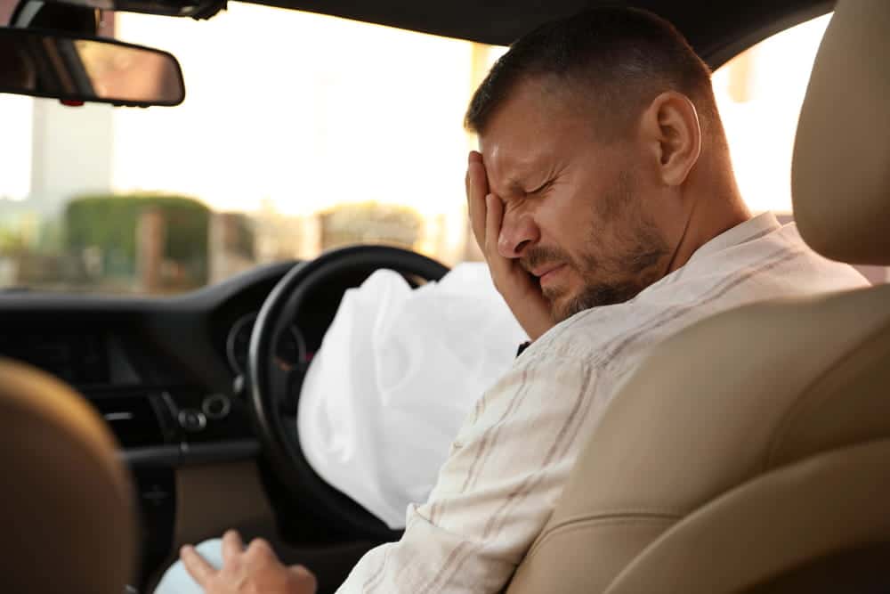 Image is of a driver experiencing head pain inside a vehicle after airbag deployment, showing head injuries that can occur in car accidents in Nashville.