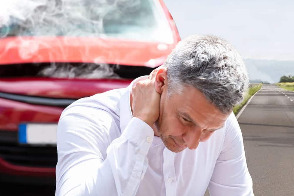 Image is of a man holding his neck near a damaged vehicle after a collision, illustrating neck injuries commonly reported in car accidents in Nashville.