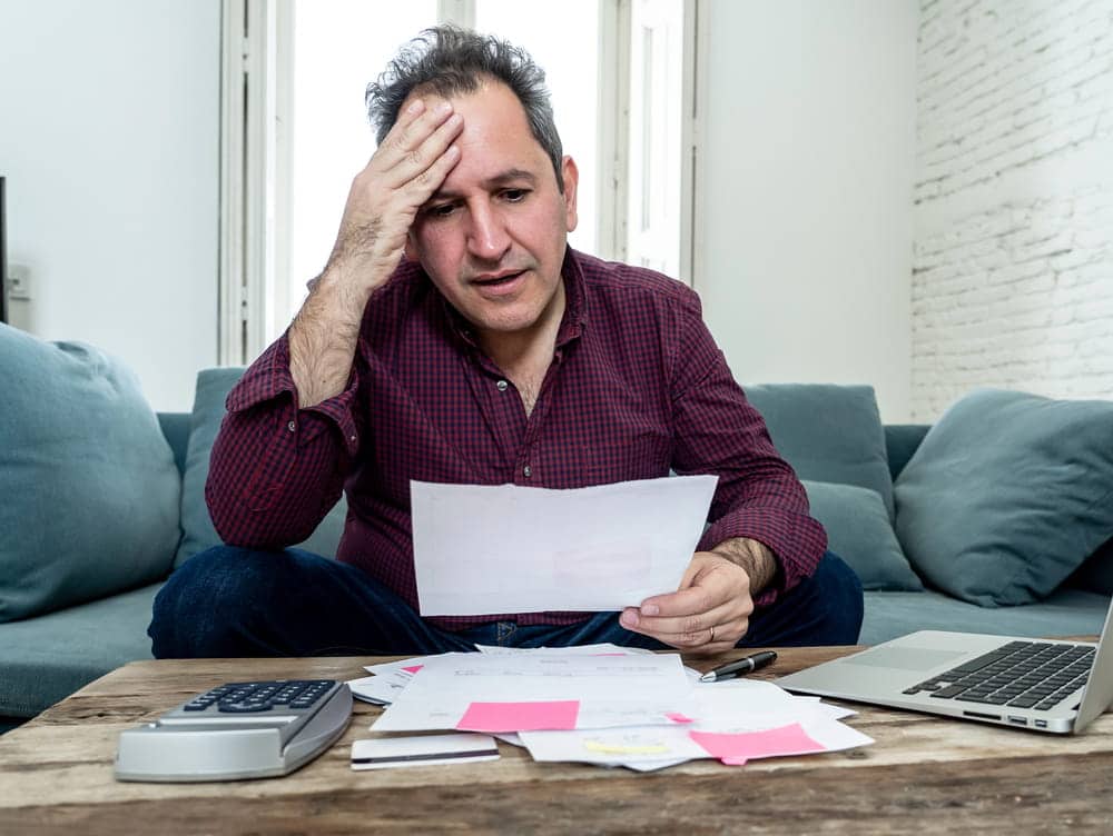 Image is of a man reviewing bills and paperwork at home, showing financial stress after an Uninsured driver accident and uncertainty about next steps.