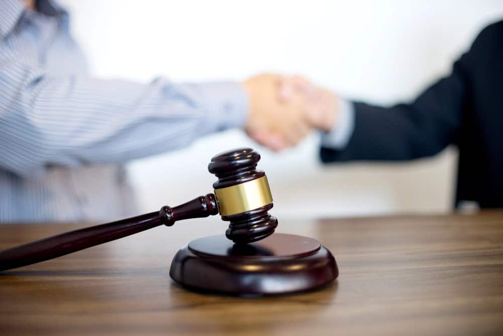 Image is of a judge gavel with two people shaking hands, concept of motorcycle accident settlement and successful legal resolution