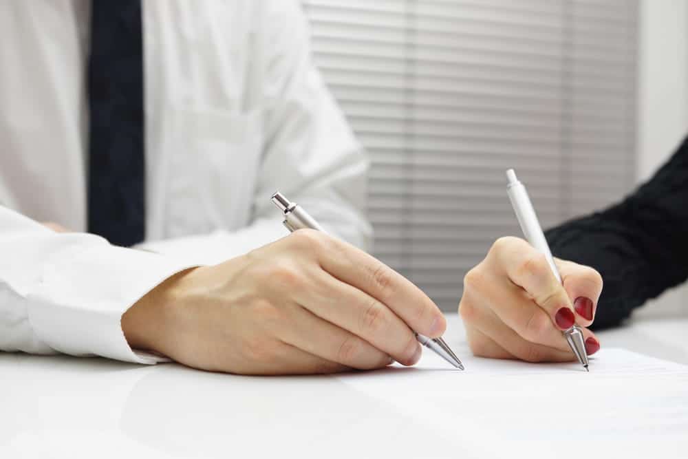 Image is of two individuals signing documents at a desk with pens, representing the process of reaching a truck accident settlement in Tennessee.