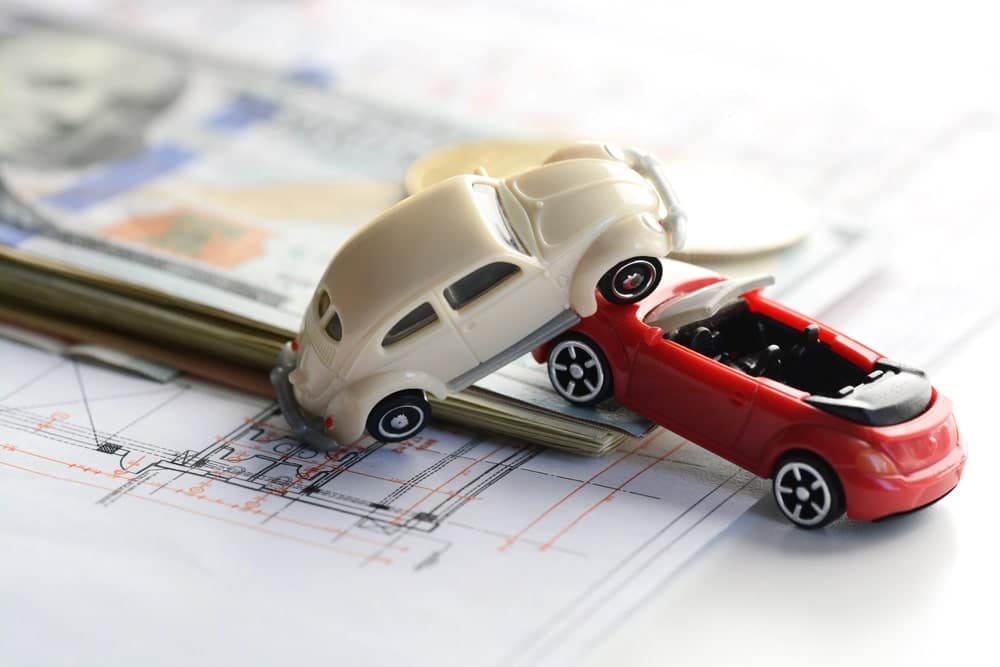 Image shows two toy cars involved in a collision placed on cash, representing financial impact after a car crash in Nashville and insurance costs