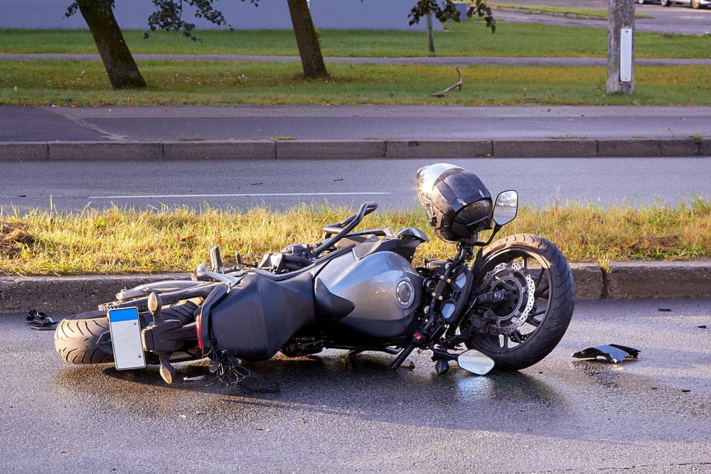 Image is of a damaged silver motorcycle lying on its side on a wet road, concept of the immediate aftermath of a motorcycle crash in Nashville.