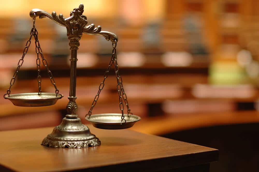 Image is of a silver decorative scale of justice on a wooden table in a courtroom, representing the legal process after a slip and fall accident.