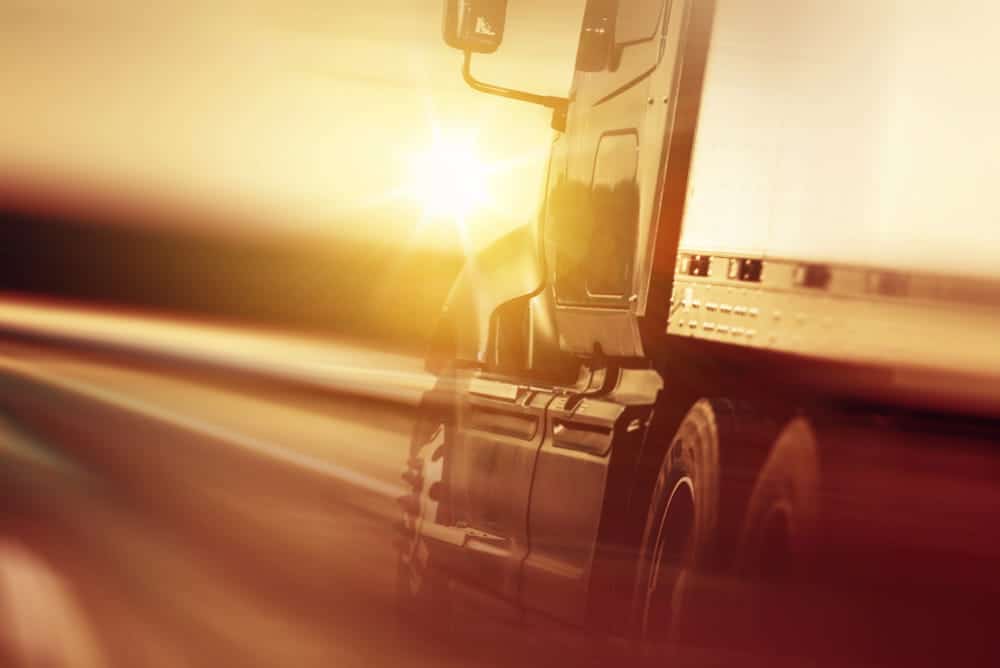 Image is of a large semi truck driving at high speed during sunset, showing the need for a truck accident lawyer