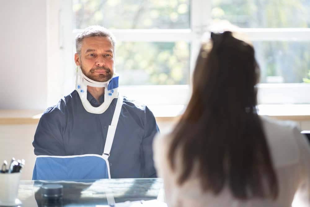 Image is of an injured man wearing a neck brace speaking with a professional, concept of truck accident injuries affecting neck and spine recovery