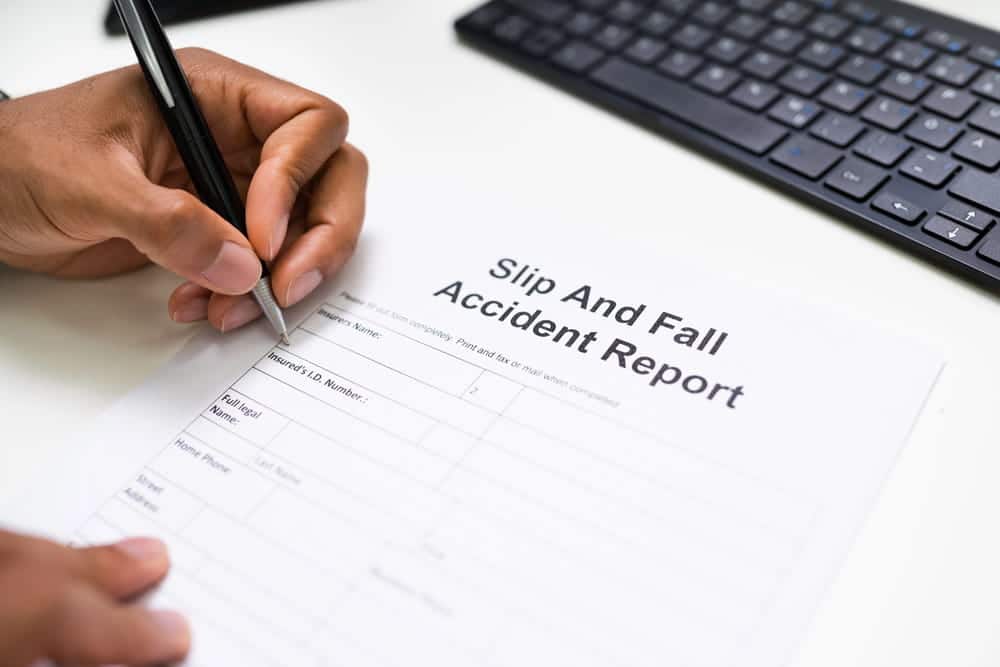 Image is of a person filling out an accident report form, concept of slip and fall at work documentation process