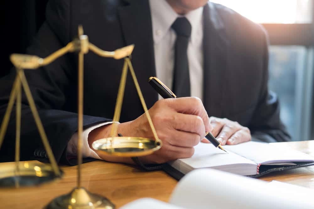 Image is of a lawyer writing notes beside a scale of justice, concept of a car accident lawyer in Nashville evaluating a claim