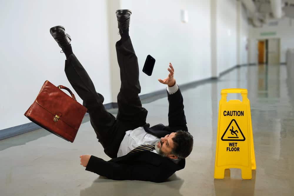Image is of a man slipping on a wet floor near a caution sign, concept of slip and fall injuries in Nashville caused by hazardous conditions