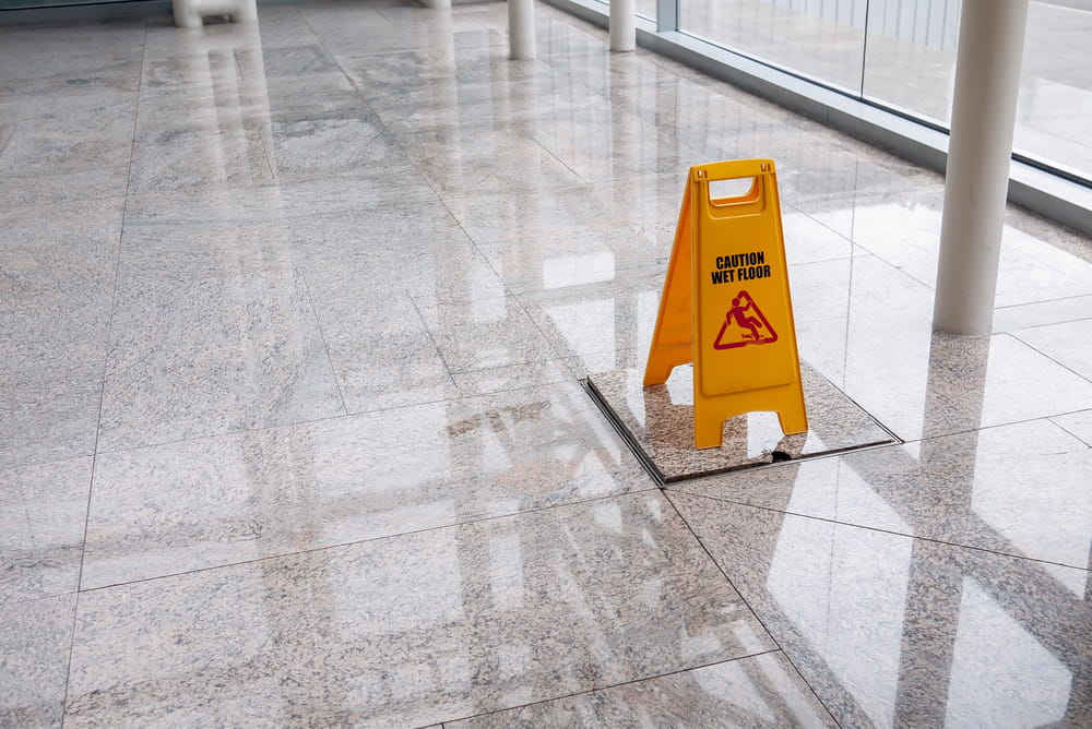 Image is of a wet floor warning sign placed on a polished hallway surface, concept of hazardous property conditions involved in Nashville slip and fall claims.