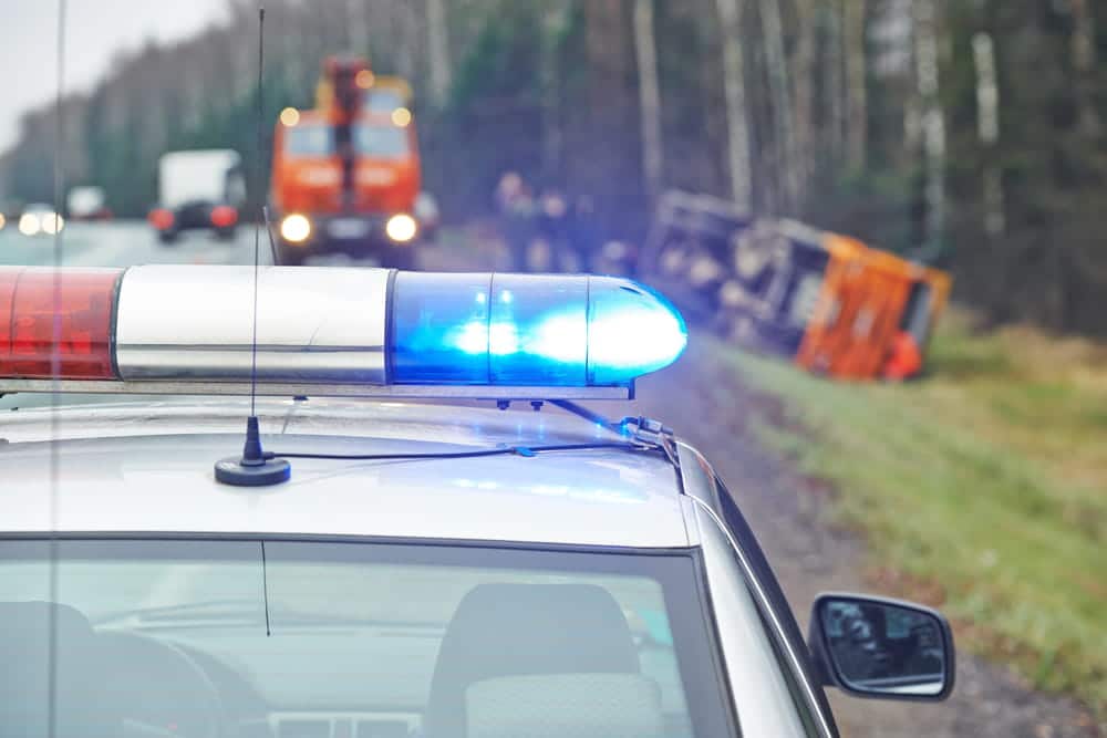 Image is of a police car with flashing lights at the scene of a Nashville crash involving an overturned truck and emergency response vehicles.