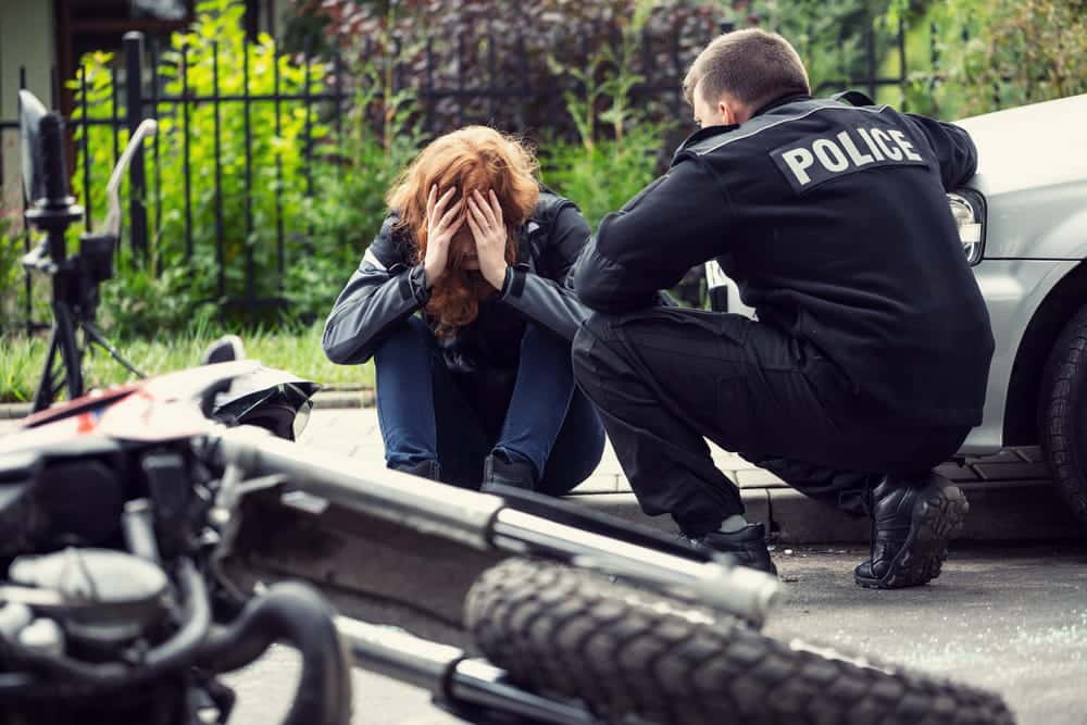 Image is of a police officer speaking with an injured rider beside a damaged motorcycle, concept of documenting injuries and scene details after a motorcycle crash.