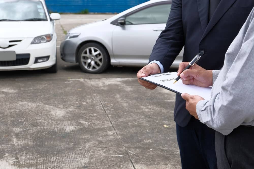 Image is of individuals reviewing documents near damaged vehicles after a collision, concept of gathering evidence and paperwork for a car accident claim within the required filing period.