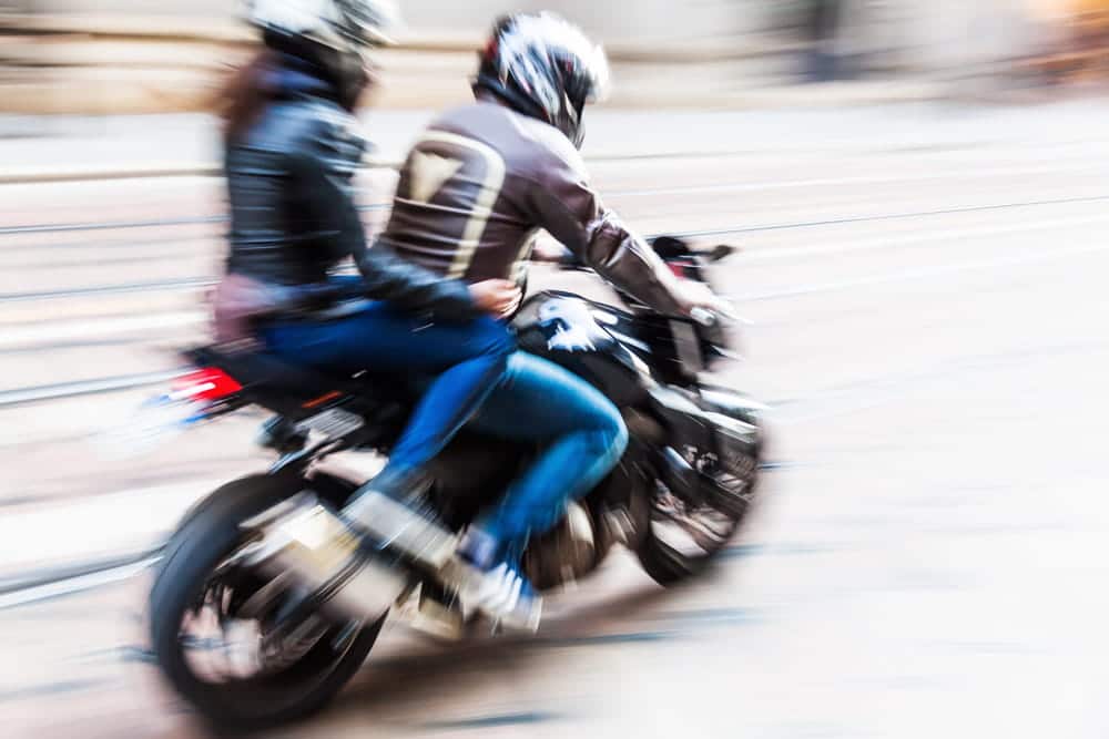 Image is of a motorcycle rider traveling with a passenger on a city street, concept of passenger injuries and legal rights after a motorcycle crash in Nashville.