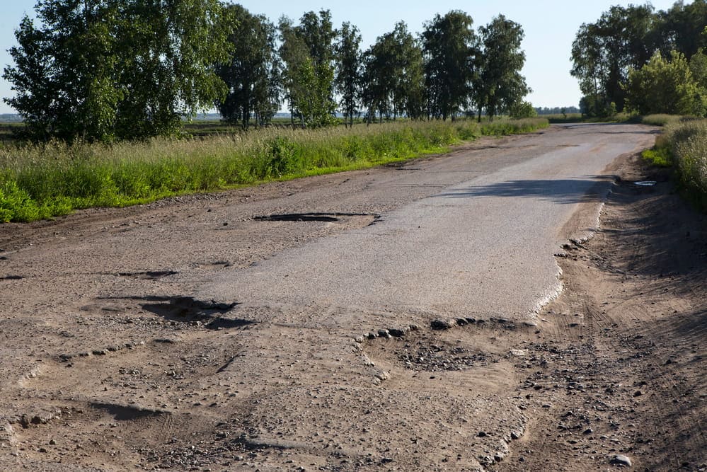 Image is of a roadway with multiple potholes and broken pavement, concept of road hazards contributing to motorcycle crashes in Nashville.