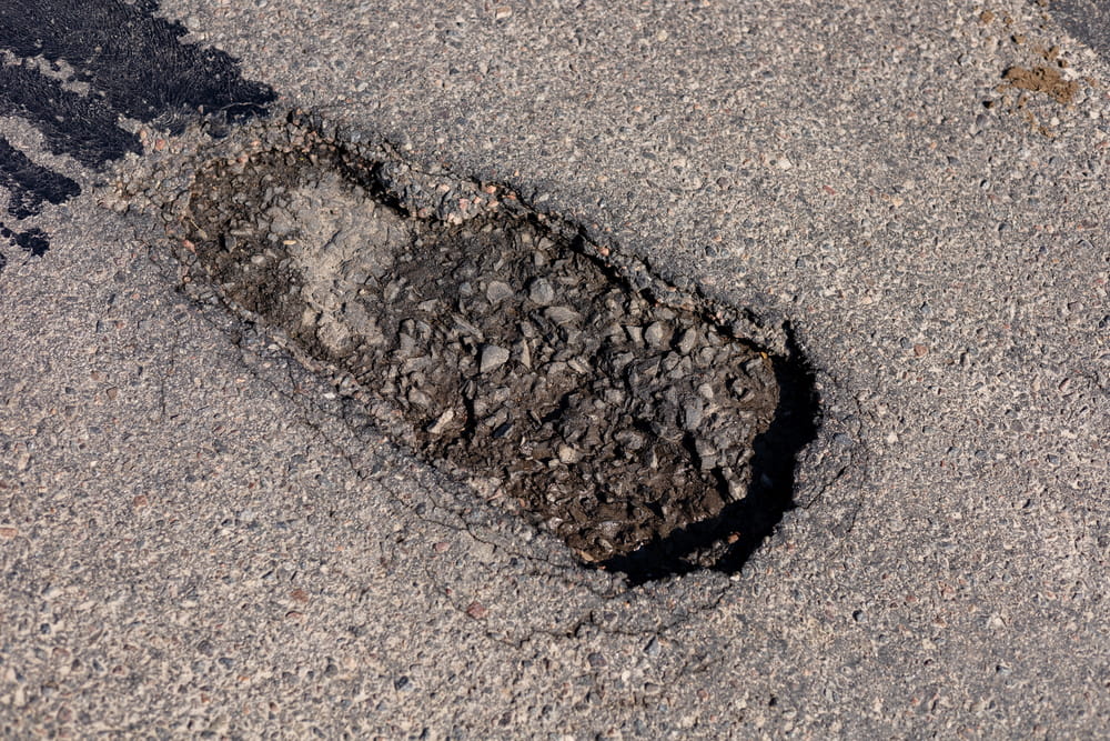 Image is of a large pothole in the pavement, concept of dangerous road conditions causing motorcycle crashes in Nashville.