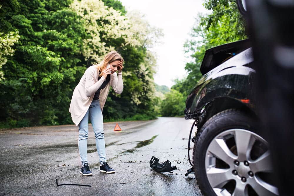 Image is of a driver standing near a damaged vehicle after a collision, concept of car accidents in Nashville involving vehicle defects.
