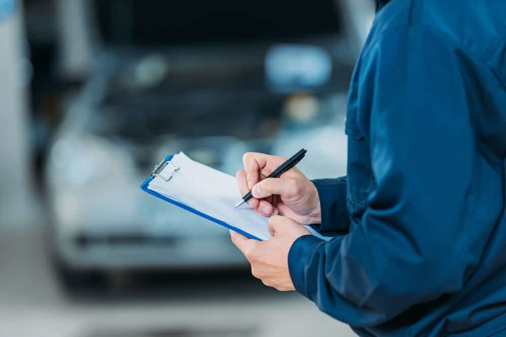 Image is of a person inspecting a vehicle with a clipboard, concept of car accidents in Nashville caused by vehicle defects.