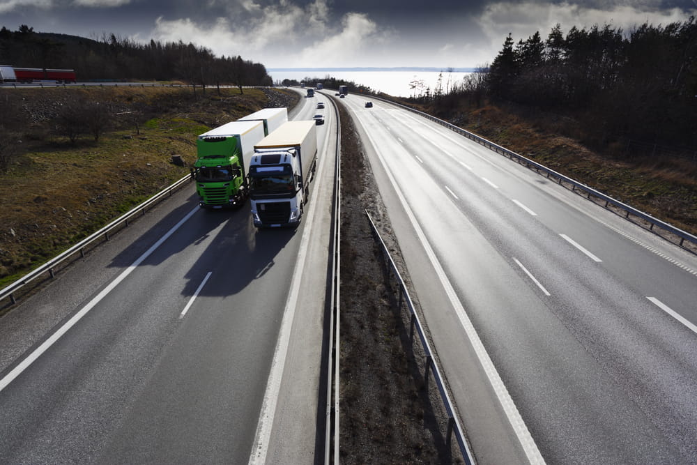 Image is of two semi trucks traveling in adjacent highway lanes, concept of semi-truck blind spot safety for nearby drivers.