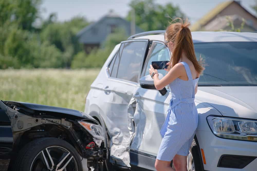 Image is of a driver photographing vehicle damage after a car crash to document the accident scene.
