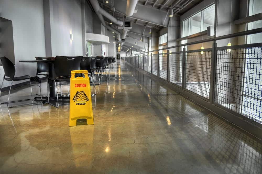 Image is of a yellow wet floor warning sign placed in a polished indoor hallway, illustrating the concept of warning signs in slip and fall injury claims.