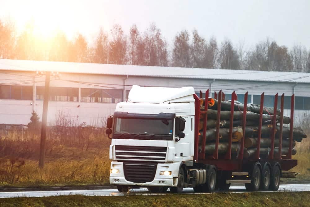 Image is of a logging truck transporting stacked timber on a wet road, illustrating how cargo securement requirements may affect a truck accident claim.