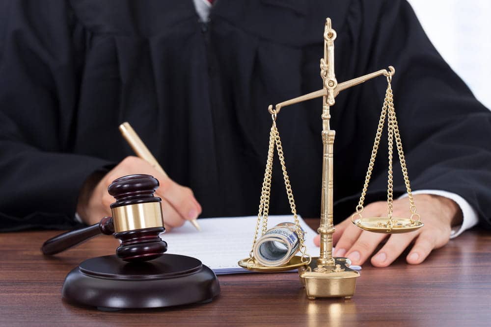 Image is of a judge writing beside a gavel and scales of justice holding money, concept of how Tennessee courts evaluate a dog bite claim.